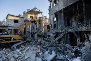 Ein Bagger hebt Trümmerteile inmitten eines eingestürzten Gebäudes. 