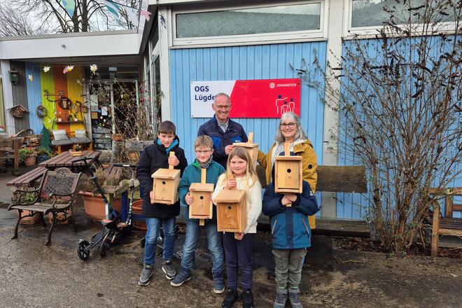 Das Bild zeigt OGS-Kinder, Spender Oliver Ernst und OGS-Mitarbeiterin Regina Siegmann vor der OGS mit Nistkästen in der Hand.