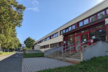Das Kita-Gebäude von außen mit Treppenaufgängen, davor ein Fußweg und eine Grünanlage.