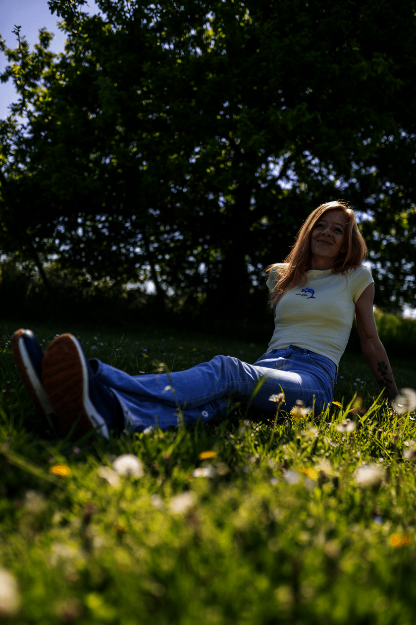 Frau sitzt entspannt auf einer Wiese, lächelt in die Sonne.  