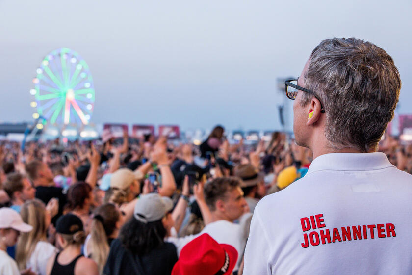 Sanitäter ist von hinten zu sehen, er blickt auf feierndes Publikum