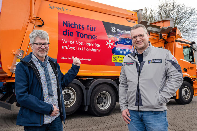 Zwei Männer vor einem Müllwagen, der beklebt ist mit "Nichts für die Tonne: Werde Notfallsanitäter (m/w/d) in Hildesheim!"