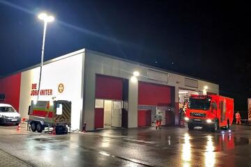 Beleuchtete Johanniter-Rettungswache bei Nacht mit Einsatzfahrzeugen vor den geöffneten Hallentoren.