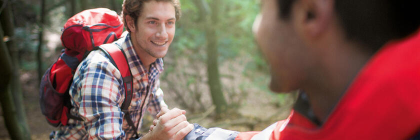 Ein Mann in Johanniter-Kleidung reicht einem anderen Menschen helfend die Hand.