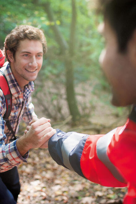 Ein Mann in Johanniter-Kleidung reicht einem anderen Menschen helfend die Hand.