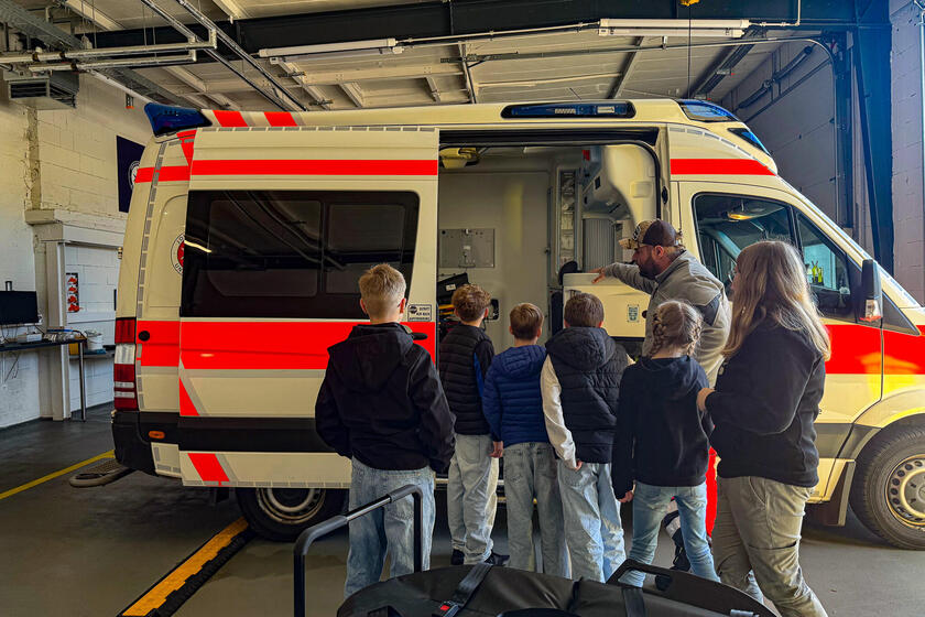 Ein Mann in Einsatzkleidung und Kinder neben einem geöffneten Rettungswagen