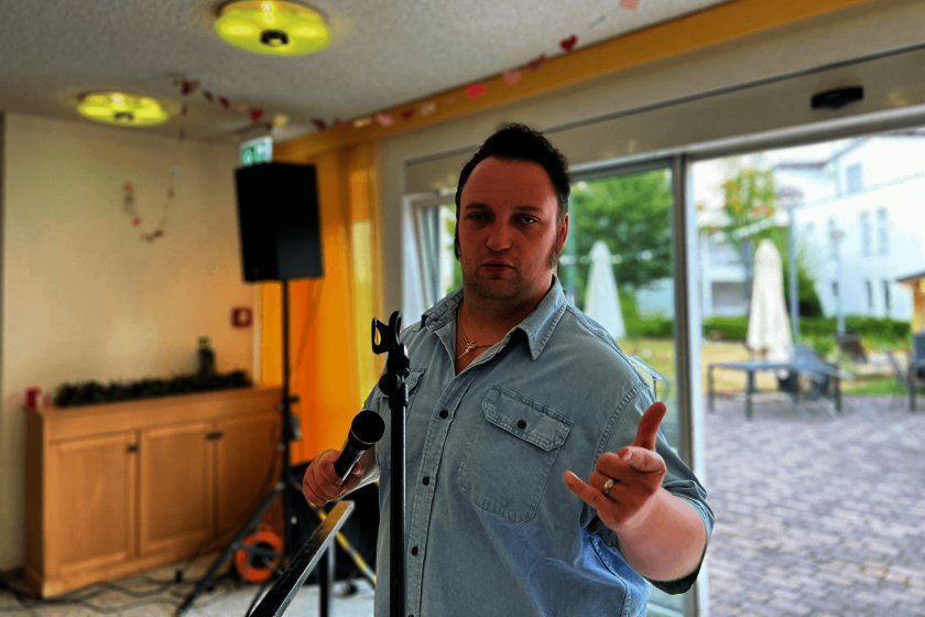 Ein Mann in einem hellblauen Jeanshemd hält ein Mikrofon in der Hand.