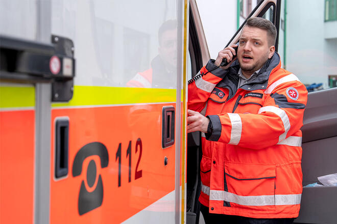 Ein Johanniter in Einsatzkleidung steht in der Tür eines Einsatzfahrzeugs und telefoniert.
