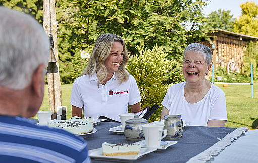 Eine Mitarbeiterin der Johanniter klärt bei Kaffee und Kuchen eine ältere Dame über die Fördermitgliedschaft der Johanniter auf