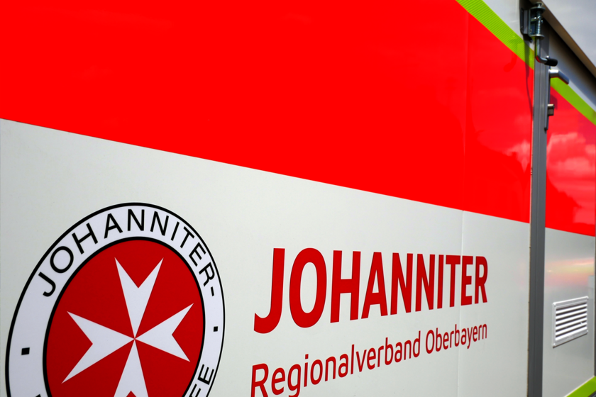 Johanniter-Logo und Schriftzug auf der roten Seitenfläche eines Einsatzfahrzeugs.