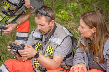 Johanniter im Einsatz bedienen im Grünen ein Steuergerät, eine Kollegin schaut aufmerksam zu.