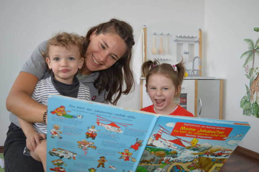 Eine Mitarbeiterin schaut ein Bilderbuch mit zwei Kindern.