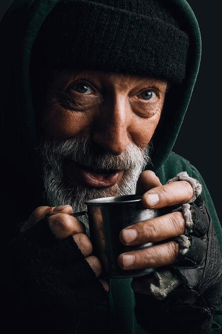 Ein Obdachloser mit einem Becher, an dem er sich wärmt