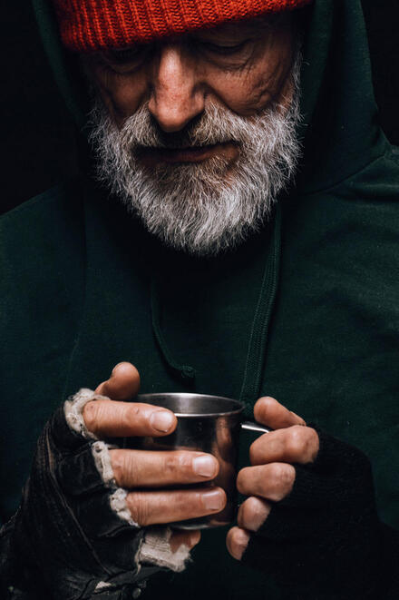 Ein Obdachloser hält einen Becher in der Hand und blickt nach unten