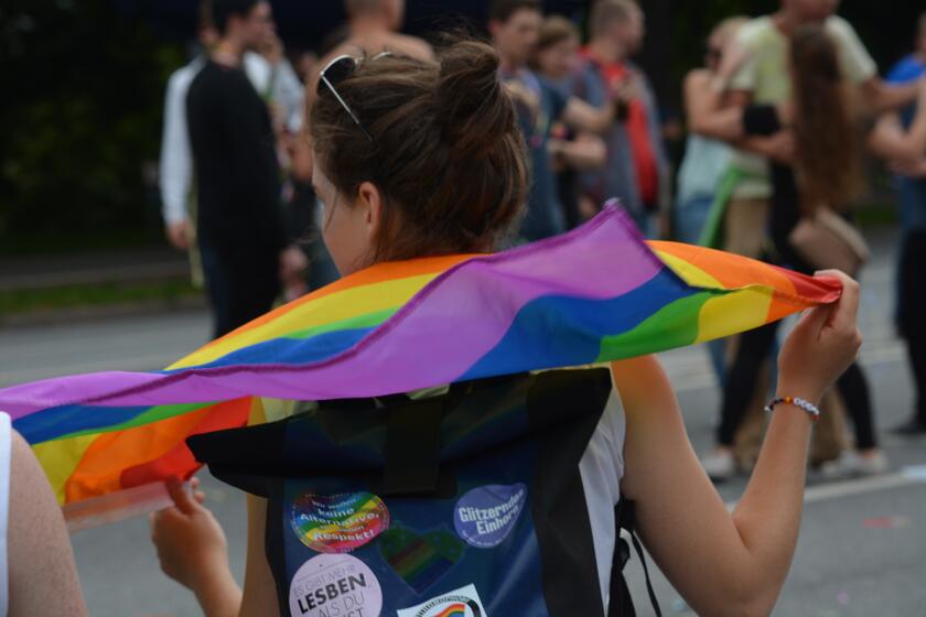 Eine Frau hält eine Regenbogenfahne über ihren Schultern.