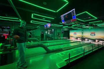 Ein Jugendlicher steht an der Bowlingbahn und hat eine Bowlingkugel in der Hand.