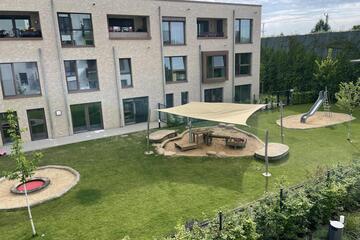 Eine Außenansicht der Kita Kunterbunt mit begrünter Fläche, Sandkästen und Rutsche.