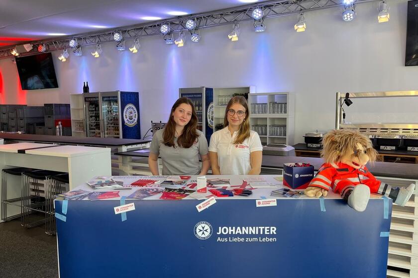 Zwei Mitarbeitende sitzen am Stand der Johanniter im Holstein Stadion.