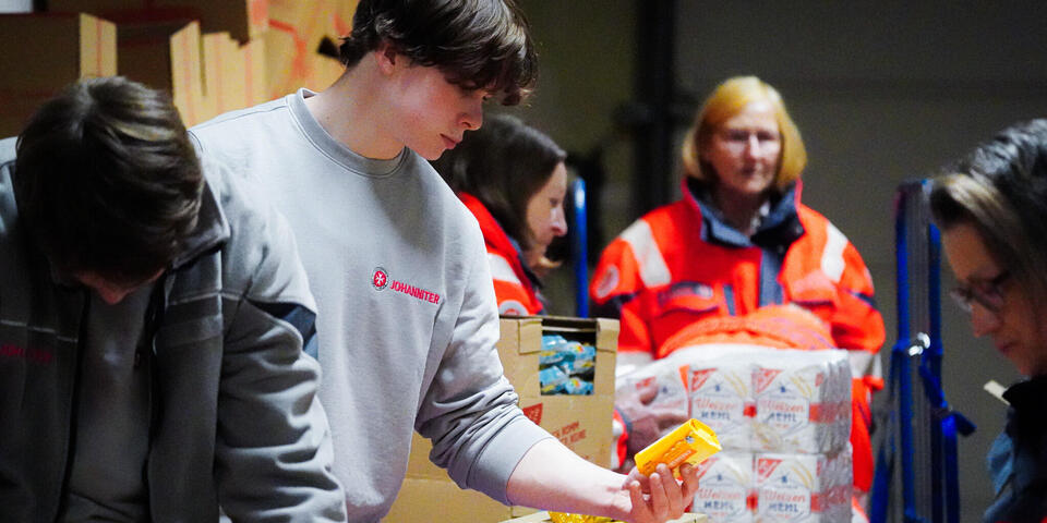 Frauen und Männer in Johanniter-Kleidung packen Lebensmittel in Pakete