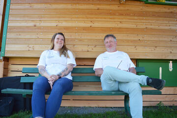 Zwei Mitarbeiter sitzen auf einer Bank vor dem Bauwagen.