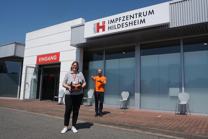 Eine Frau mit einem Radio und ein Mann vor einem Impfzentrum