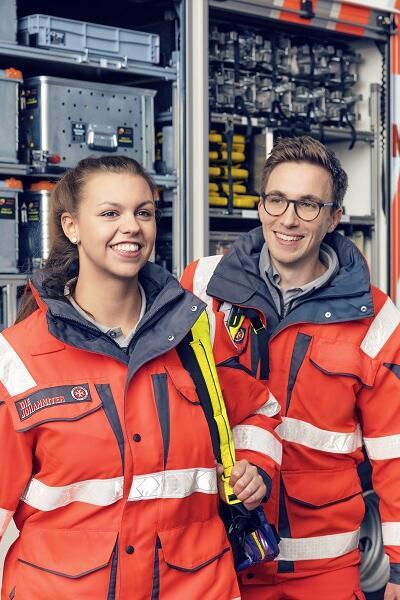 Zwei Ehrenamtliche der Johanniter vor einem Einsatzwagen