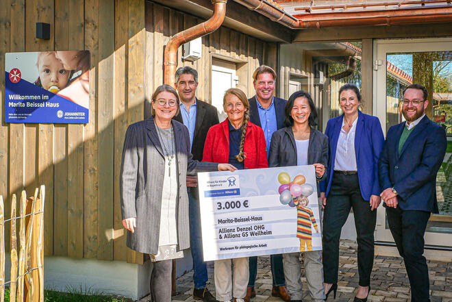 Mehrere Leute stehen vor einem Gebäude und halten einen großen Spendencheck für das Marita-Beissel-Haus der Johanniter.