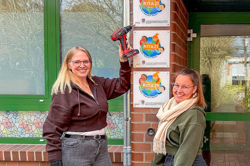 Jennifer Meyer und Lina Ködder, Mitarbeitende der Oeringer Strolche, bringen die mittlerweile dritte Plakette neben der Eingangstür an.