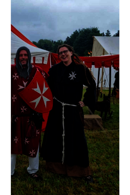 Frau in historischer Gewandung aus dem Mittelalter steht auf einer Wiese.