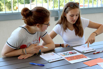 Zwei Mädchen diskutieren über Arbeitsblätter und Mitschriften, die vor ihnen liegen.