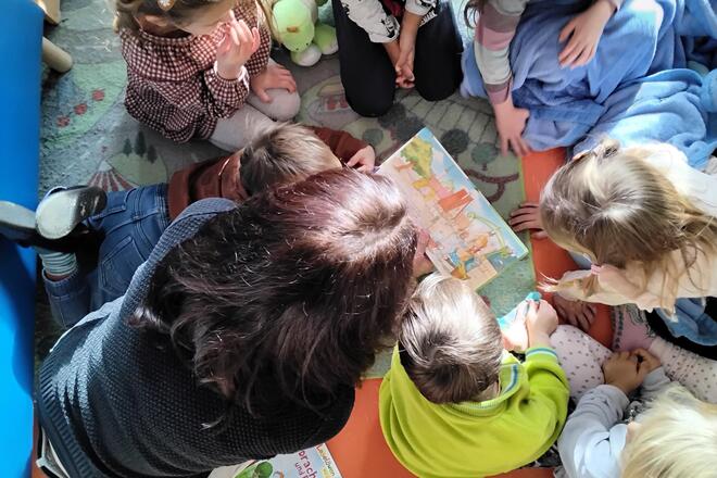 Eine Mutter ließt mehreren Kindern etwas vor.