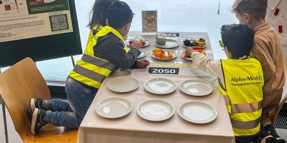 Vier Kinder, drei davon mit gelber Warnweste an einem Tisch mit Tellern.