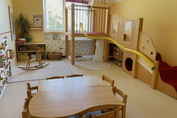 Ein Raum mit einer hölzernen zweistöckigen Spieleplattform, Schaukelpferd und Tisch und Stühlen.