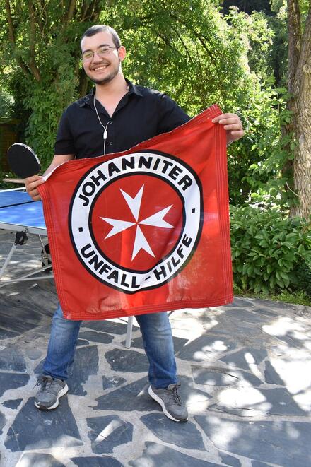 Junger flüchtling mit Johanniter Fahne im Garten der Waldracher Einrichtung.