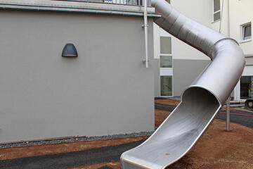 Silberfarbene Rutsche die vom Obergeschoss ins Erdgeschoss führt. 