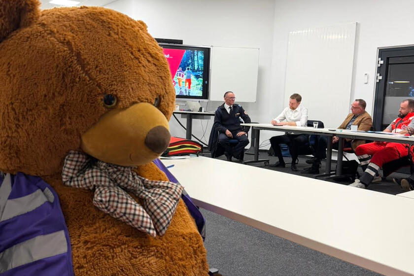 Im Vordergrund ist das Maskottchen, der PSNV-Teddy zu sehen und im Hintergrund Herr Kretschmer im Austausch mit den Ehrenamtlichen