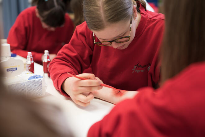 Jugendmitglied der Johanniter schminkt eine realistische Wunde auf einem Arm.