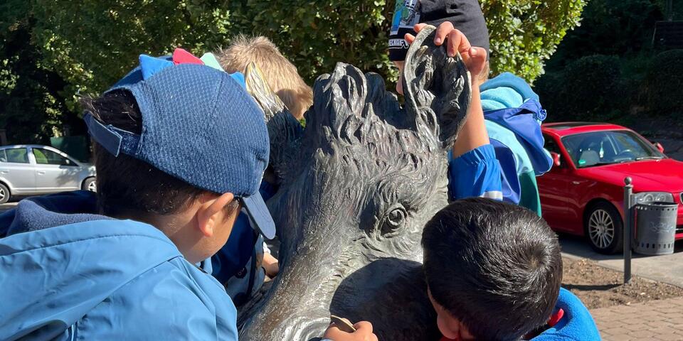 Kinder umarmen eine Wildschweinstatue