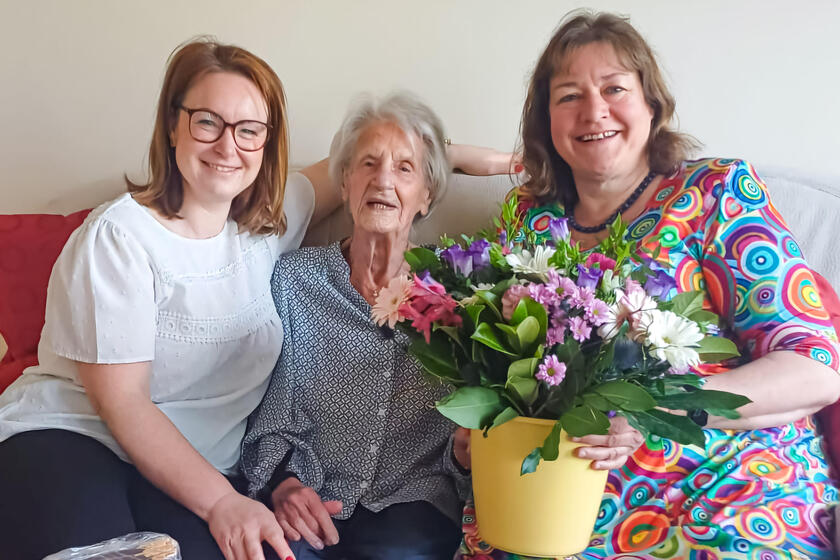 Zwei Mitarbeiterinnen der Johanniter gratulieren einer älteren Dame in der Mitte zu ihrem Geburtstag.