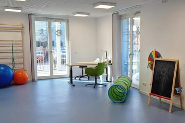 Bild vom Bewegungsraum der Praxis mit Klettersprossen, Bällen, Kriechtunnel und anderen Spielgeräten