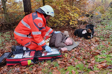 Rettungshelfer kniet neben verletzter Person und versorgt diese