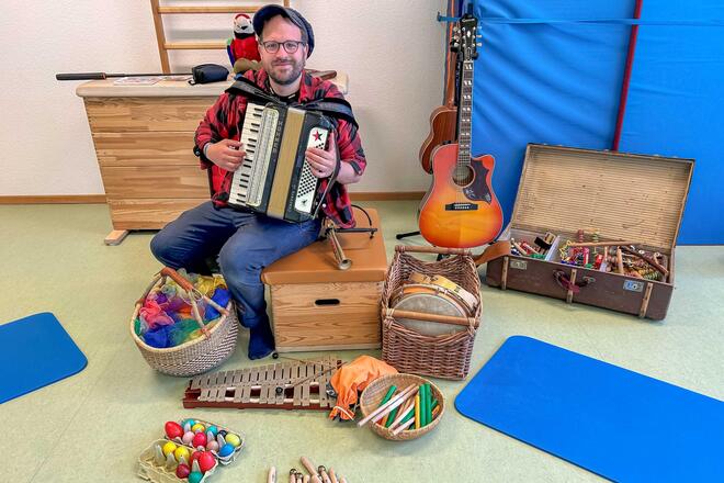 Krippenkonzerte in der Johanniter-Kita Stoppelhopser Musikpädagoge Lukas Johannsen hat ein Akkordeon in der Hand und sitzt vor einer großen Auswahl von verschiedenen Instrumenten im Bewegungsraum der Kita.