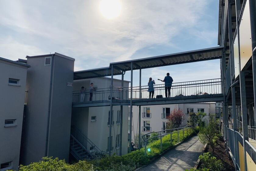 Auf einem Steg zwischen den Gebäuden stehen oben die Musikerin und der Musiker.