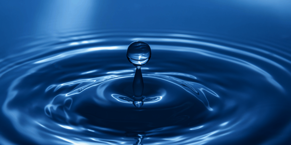 Ein Tropfen fällt auf eine Wasseroberfläche. Das ganze Bild ist blaugefärbt.