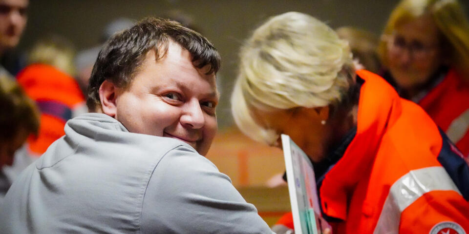 Ein Mann lächelt in die Kamera. Hinter ihm packen Menschen Pakete