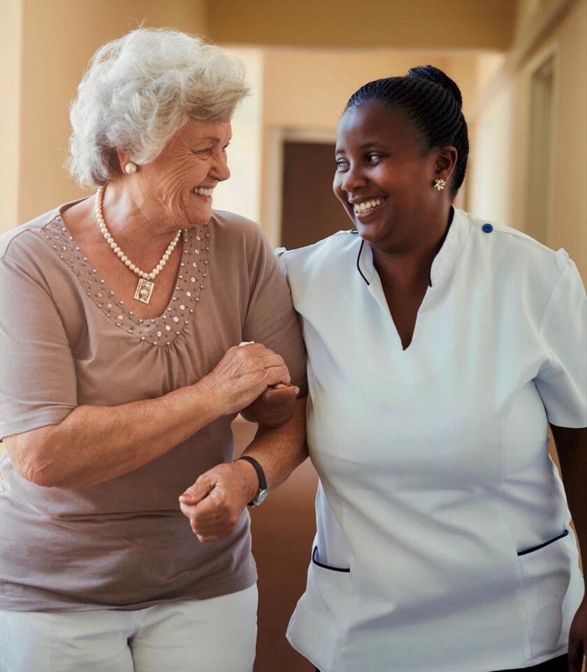 Junge Frau mit Migrationshintergrund unterstützt ältere Dame.