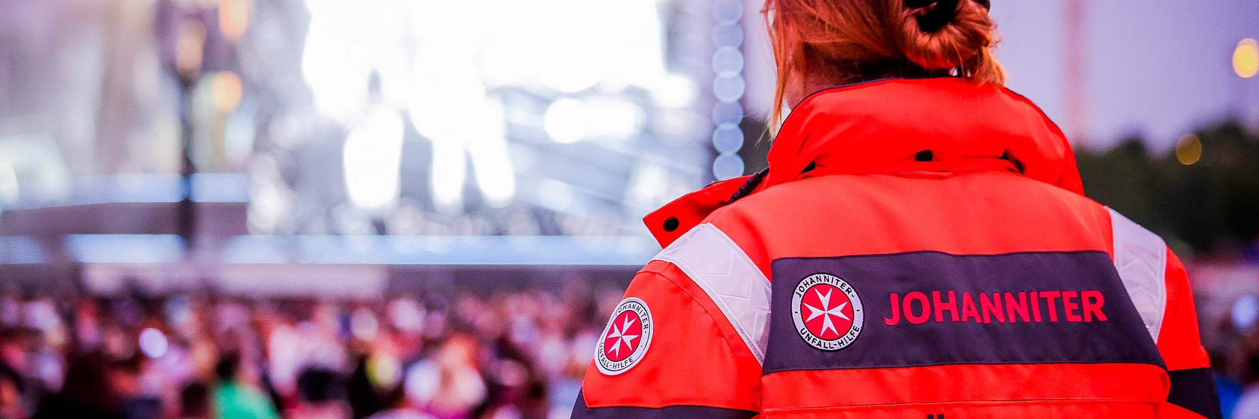 Eine Johanniter-Sanitäterin beobachtet von hinten die Menschenmenge bei einer Großveranstaltung und ist für den Sanitätsdienst im Einsatz.