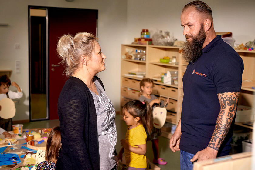 Johanniter Mitarbeiter berät eine Mutter, Kinder basteln im Hintergrund.