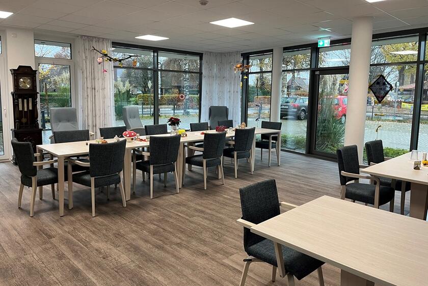 Mehrere Tische und Stühle in einem hellen, mit großen Fenstern ausgestattetem Raum der Tagespflege