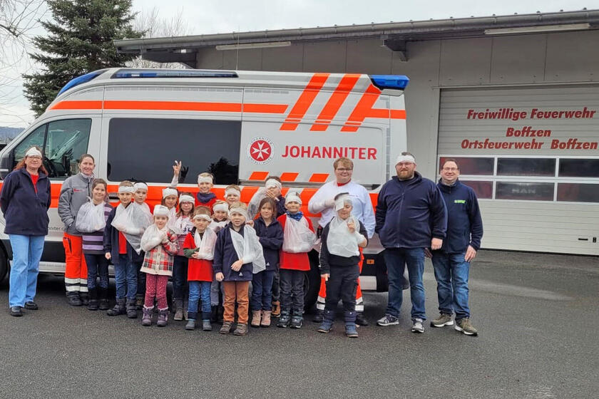 Kinder und Erwachsene mit Verbänden vor einem Rettungswagen
